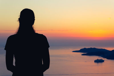 Silhouette woman standing by sea against orange sky