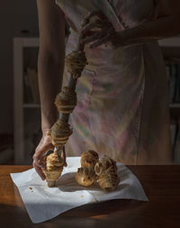 An unrecognisable woman is pulling freshly baked home-made puff pastry cannoli from a wooden stick.