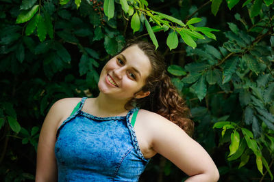 Portrait of teenage girl wearing tank top while standing against plant
