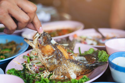 Hand touches the fish on a dish waste food after eating a cooked fish, unclean