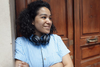 Smiling woman with headphones leaning in front of wooden door