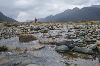 Stones by stream against cloudy sky