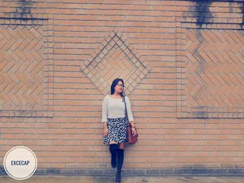 Full length portrait of teenage girl standing against brick wall