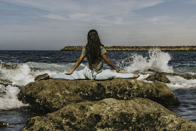 Man sitting on rock at sea shore against sky