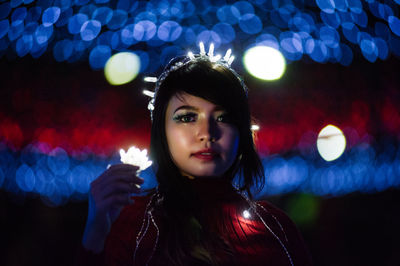 Portrait of young woman with illuminated lighting decoration at night