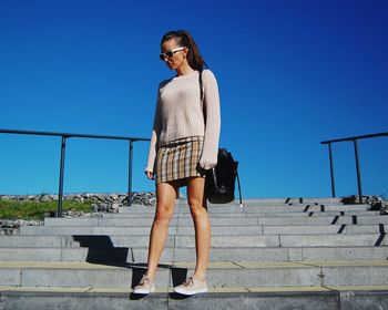 Low angle view of woman standing on steps against clear blue sky
