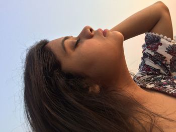 Side view of young woman with eyes closed against clear sky