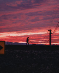 Silhouette person standing by electricity pylon against sky during sunset