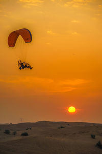 Silhouette person paragliding against sky during sunset