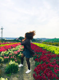 Woman tossing hair while standing by flowering plants against sky