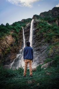 Rear view of boy looking at waterfall in forest