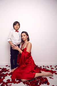 Mother in a red dress is sitting on the floor with a child, son in rose petals on valentine's day
