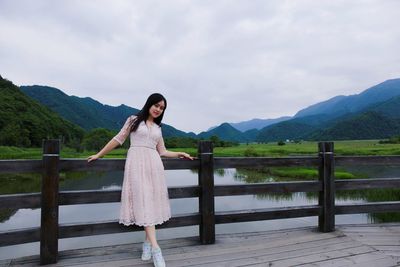 Portrait of woman standing on footbridge over lake