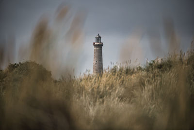 Lighthouse by field against sky