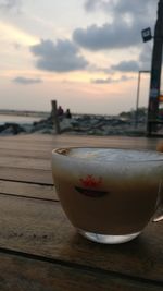 Close-up of beer on table against sea during sunset