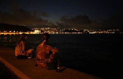 Young woman sitting on illuminated cityscape against sky at night