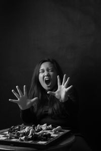 Portrait of young woman sitting against black background