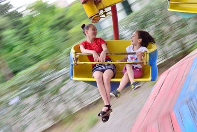 Blurred motion of cheerful girls sitting in carousel