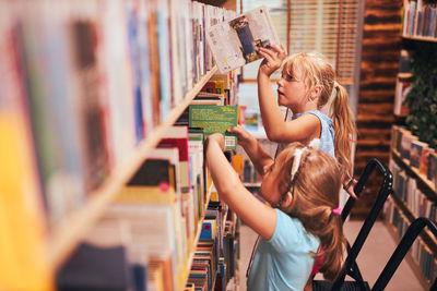 Schoolgirls looking for books in school library. students choosing set books. elementary education