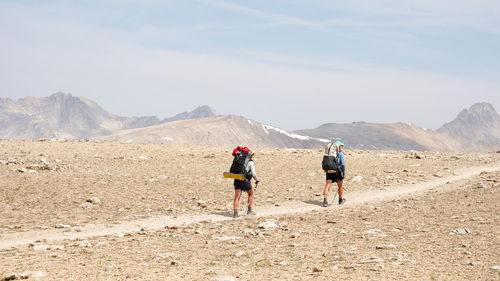 Rear view of people walking on mountain road against sky