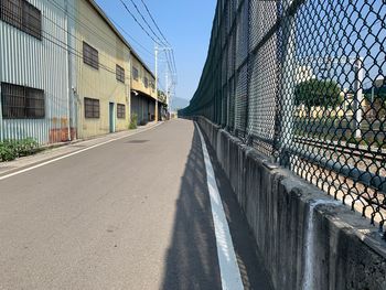 Empty road amidst fence against sky