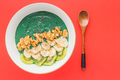 A spirulina smoothie bowl with banana, walnuts, kiwi and chia seeds on red background