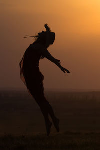 Silhouette woman dancing against orange sky during sunset