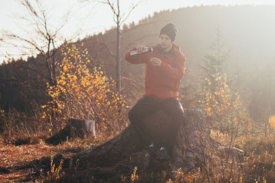 Tourist sitting on a fire pouring hot tea from a thermos into cup at sunrise. beskydy czech republic