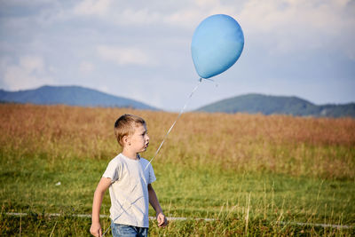 Full length of boy holding balloons on field against sky