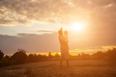 Rear view of man standing on field against sky during sunset