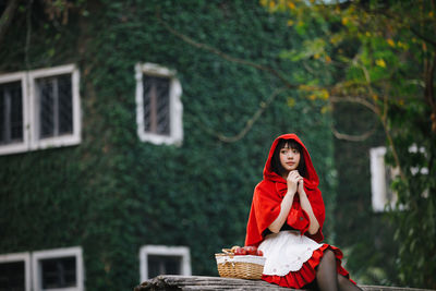 Young woman with fruits in basket looking away while sitting against house