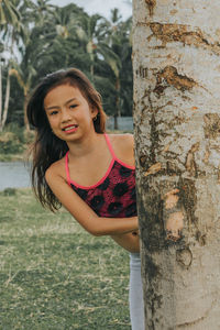 Portrait of a smiling young woman against tree trunk