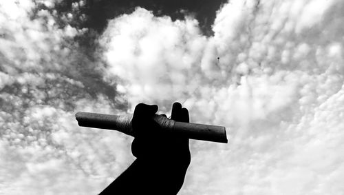 Low angle view of silhouette person holding cross against sky