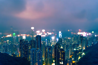 Tilt shift image of illuminated cityscape against cloudy sky at night