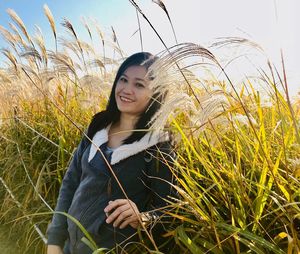 Portrait of smiling mid adult woman standing on grassy field against sky