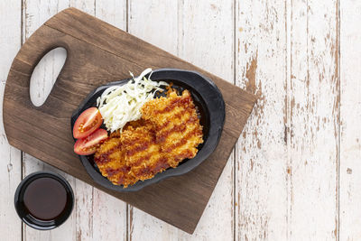 Japanese deep fried pork cutlet or tonkatsu with sauce, cabbage and tomato in black ceramic plate 