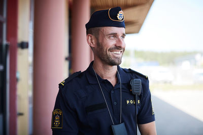 Happy policeman looking away while standing outside police station