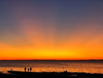 Silhouette people at beach against sky during sunset