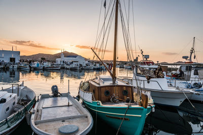 Sailboats moored in harbor at sunset