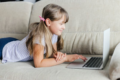 The girl lies on the sofa at home and uses a laptop. teaching children at home. online  home school.