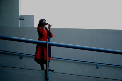 Full length of woman photographing while standing by railing