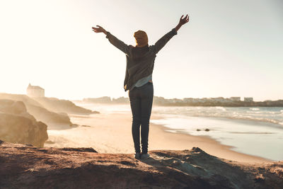 Rear view of woman standing on rock at beach against sky