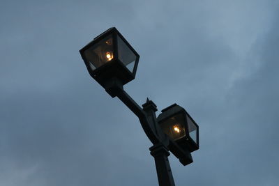 Low angle view of illuminated street lights against cloudy sky