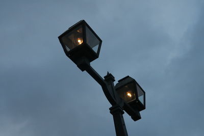 Low angle view of illuminated street lights against cloudy sky