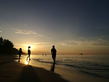 Silhouette people standing at beach against sky during sunset