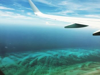 Aerial view of airplane wing over sea against blue sky