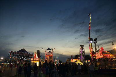 People at illuminated amusement park against sky