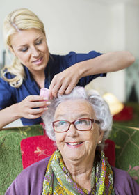 Female caretaker putting curlers to senior woman's hair at nursing home