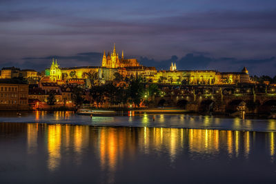 Prague castle and charles bridge lit up at night with the lights reflecting on the vltava river.