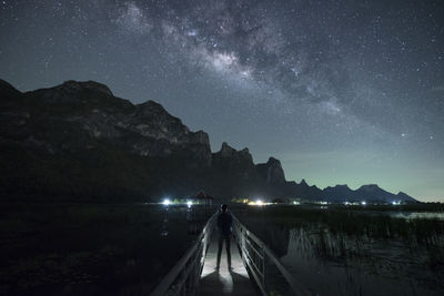Man standing on footbridge over lake against sky at night